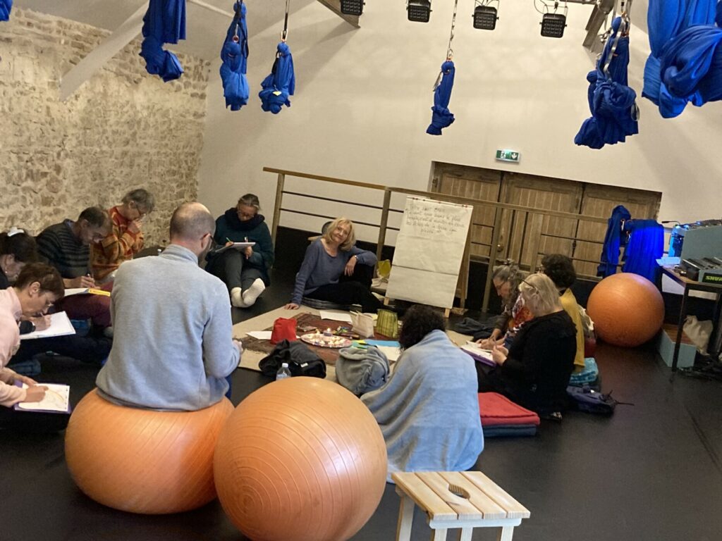Jardin au naturel Plusieurs personnes dans une salle avec des hamacs suspendus, des ballons de gym et des tapis. Ils discutent ensemble en cercle
